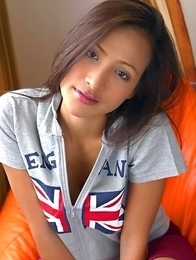 Teaza Tsing sits down on an orange sofa with a zip up England t shirt on.