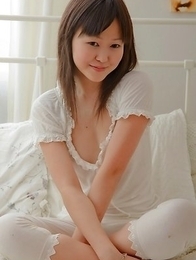 Aliana is sitting on her bed wearing white and smiling at the camera.